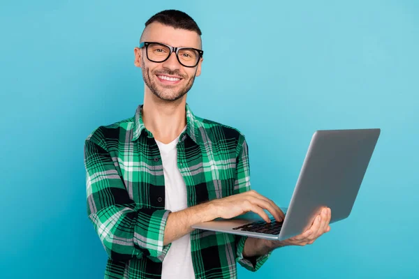 Foto av glad ung positiv man ser hålla handen laptop gott humör leende avslappnad isolerad på blå färg bakgrund — Stockfoto