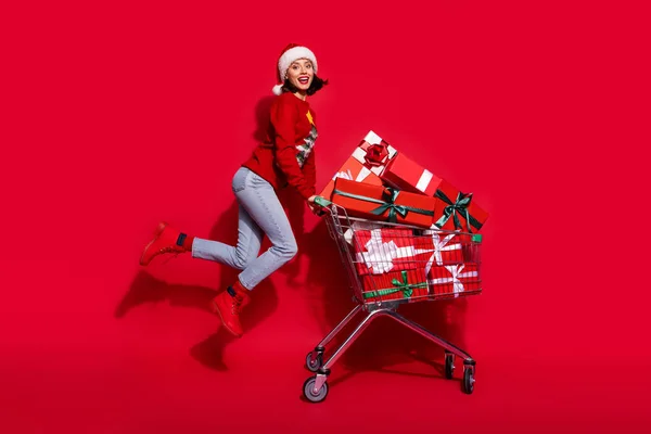 Photo de doux drôle jeune femme porter pull imprimé sautant acheter de nouveaux cadeaux de l'année souriant isolé fond de couleur rouge — Photo