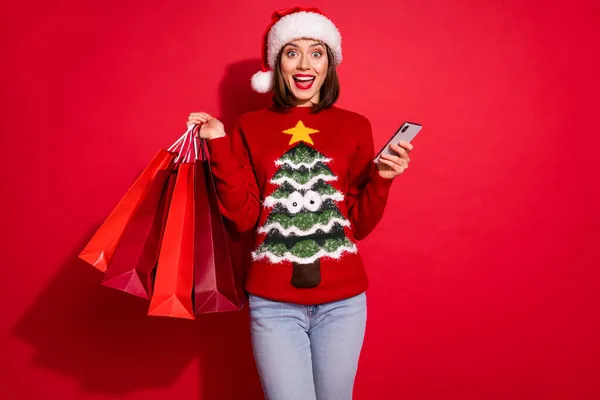 Fénykép izgatott vicces fiatal hölgy öltözött nyomtatott pulóver vásárol újévi ajándékok csevegés modern szerkentyű elszigetelt piros szín háttér — Stock Fotó