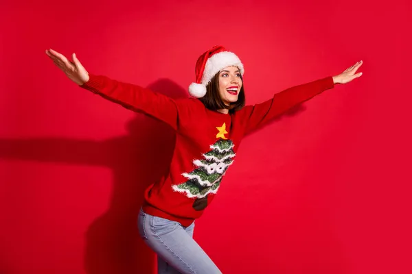 Foto de menina bonito infantil vestido pulôver de impressão de natal segurando lados braços olhando espaço vazio isolado cor vermelha fundo — Fotografia de Stock