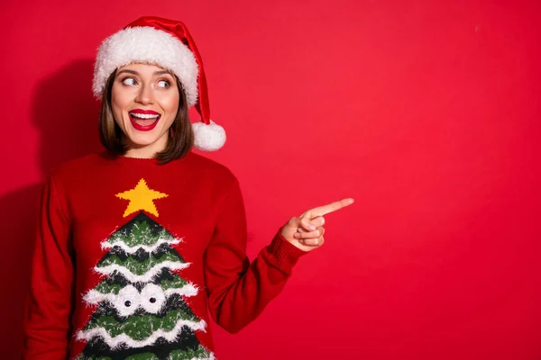 Photo de douce excitée jeune femme habillée pull impression appréciant Noël pointant doigt espace vide sourire isolé fond de couleur rouge — Photo