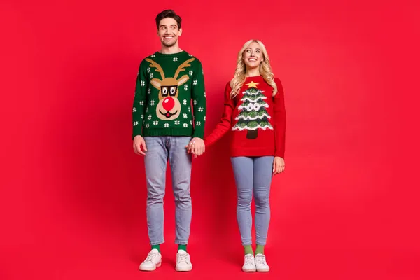 Photo of excited dreamy curious couple hold hands empty space wear ugly sweater jeans shoes isolated red color background — Stock Photo, Image