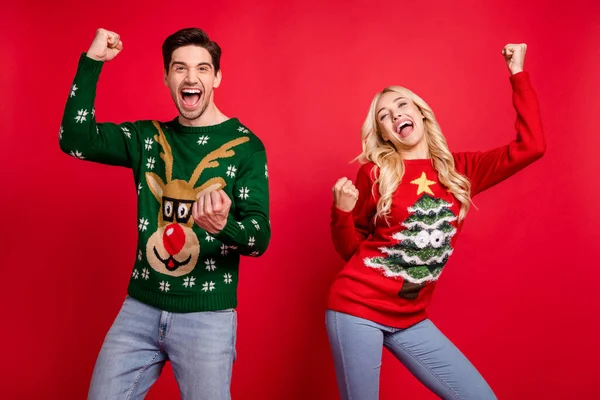 Photo of astonished couple celebrate victory scream goal raise fists wear ugly sweater isolated red color background — Stock Photo, Image