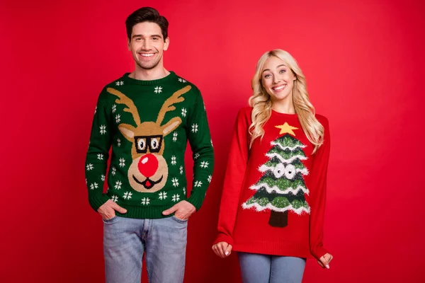 Photo portrait happy smiling couple wearing ugly sweaters celebrating winter holidays isolated vivid red color background — Stock Photo, Image