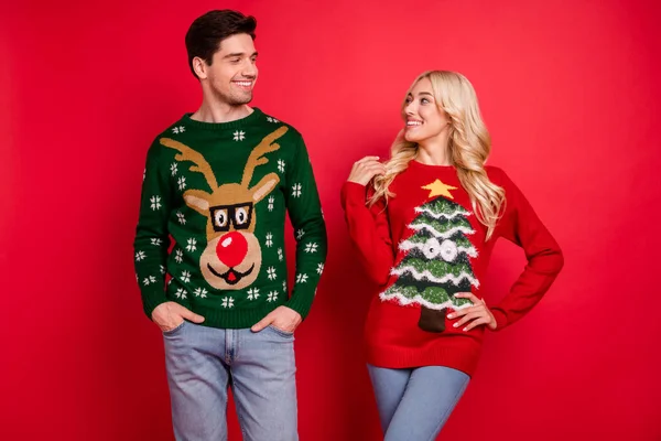 Photo portrait smiling couple wearing ugly sweaters celebrating xmas isolated bright red color background — Stock Photo, Image