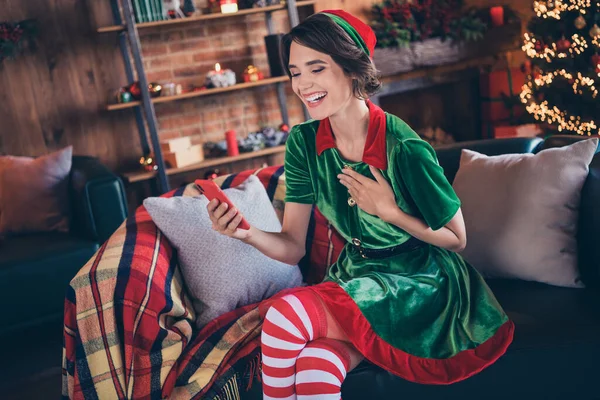 Foto de alegre alegre feliz mulher santa ajudante segurar as mãos telefone sentar sofá natal humor xmas dentro de casa casa — Fotografia de Stock