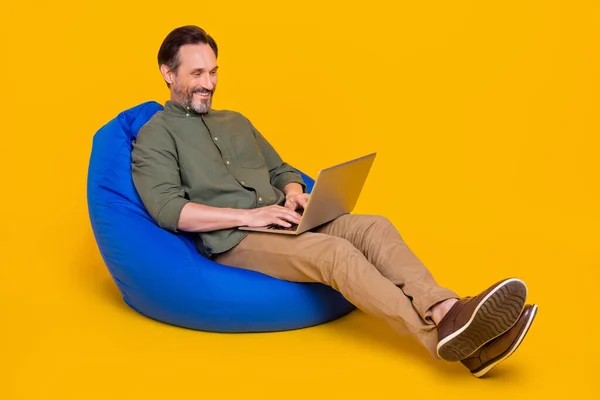 Portrait of attractive cheerful man sitting in chair using laptop programming web isolated over bright yellow color background — Stock Photo, Image