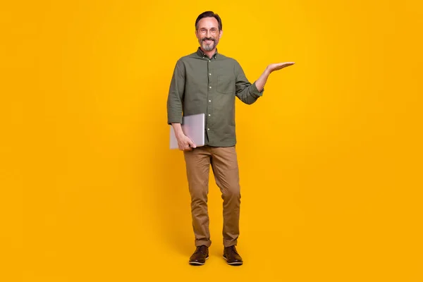 Teljes hosszúságú fotó érett férfi boldog pozitív mosoly hold laptop kéz termék reklám promo elszigetelt sárga szín háttér — Stock Fotó