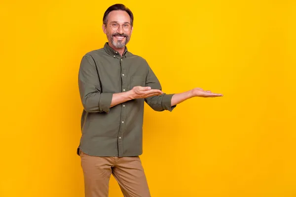 Портрет привабливого веселого чоловіка, який тримає на долонях копіювати рекламний простір ізольовано на яскраво-жовтому кольоровому фоні — стокове фото