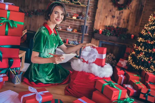 Фотографія молодої щасливої шокованої щасливої дівчини-помічника Санти робить список подарунків всередині будинку будинку — стокове фото