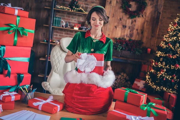 Фото позитивної дружньої веселої леді готують мішкові подарунки в костюмі ельфа в декорованому офісі в приміщенні — стокове фото