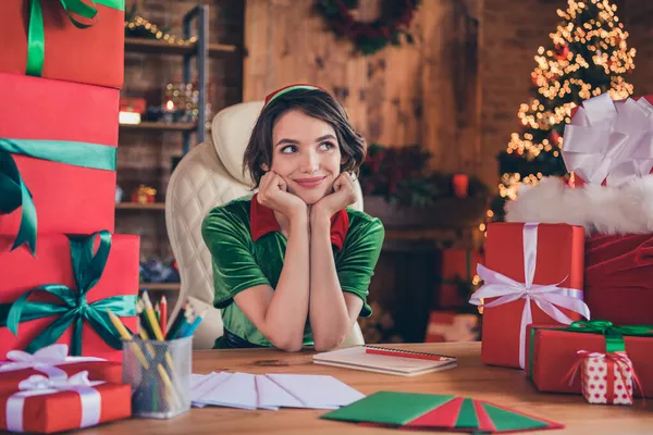 Fotografie mladé snivé pěkné šťastný Santa pomocník žena sedět stůl ruce tvář vzhled Představte si, uvnitř domu doma — Stock fotografie