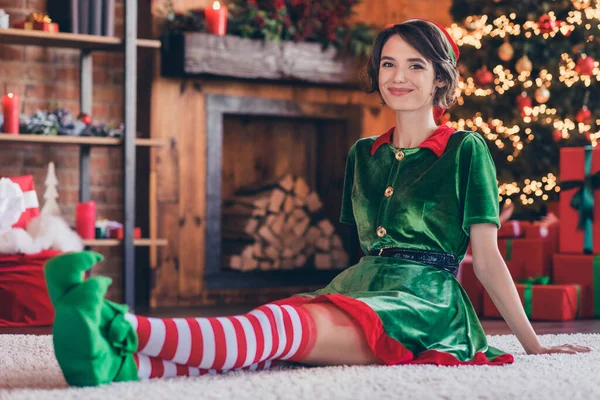 Foto de engraçado doce jovem mulher vestida verde traje sorrindo celebrando o ano novo sentado chão dentro de casa quarto casa — Fotografia de Stock