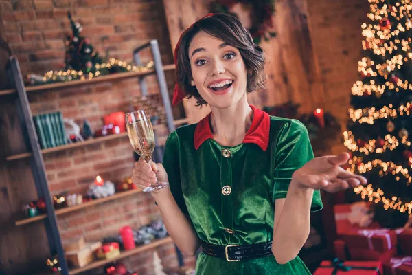 Фото молодой девушки, одетой в зеленый костюм и улыбающейся, празднующей Новый год, пьющей шампанское в помещении дома — стоковое фото