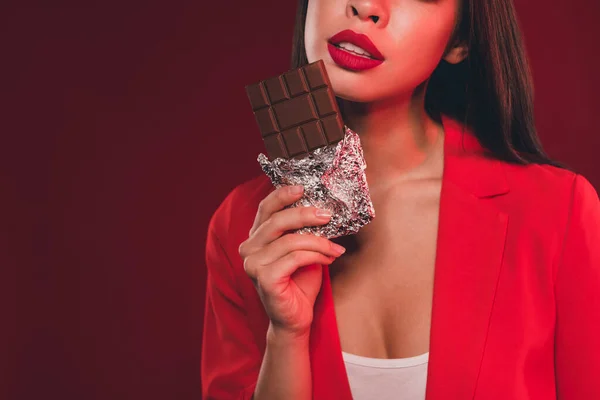 Vedere decupată portret de fată atrăgătoare superba mananca negru ciocolata junk nutritie izolat peste roșu lumina stralucire culoare fundal — Fotografie, imagine de stoc