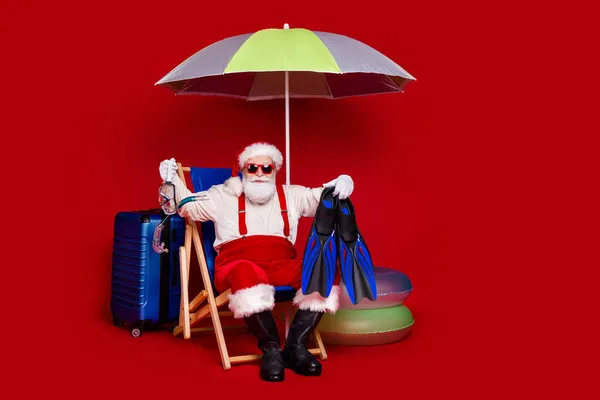 Photo of fat excited man pensioner dressed santa claus costume sitting deck chair enjoying vacation smiling isolated red color background — Stock Photo, Image