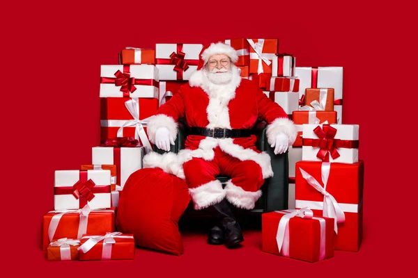 Foto van grappige vrolijke gepensioneerde man dragen kerstman kostuum bril glimlachen voorbereiding van nieuwjaar presenteert geïsoleerde rode kleur achtergrond — Stockfoto