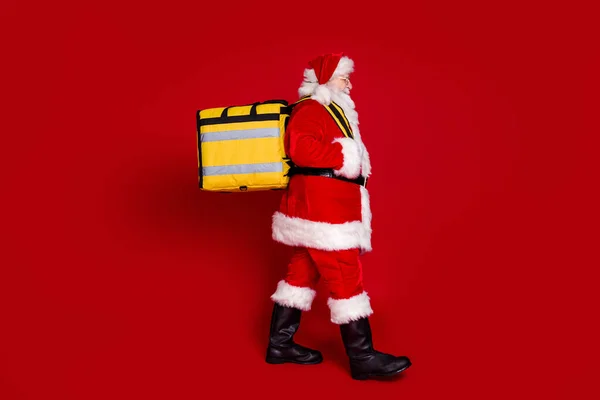 명랑 한 남자 연금 생활 자의 사진 산타 클로스 복장을 입고 걸어오는 모습붉은 색 배경에 웃으며 배달 배낭을 메고 가는 모습 — 스톡 사진