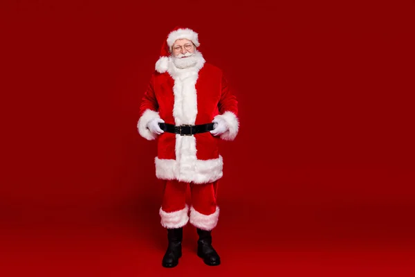 Foto van vrolijke leuke man gepensioneerde gekleed santa claus kostuum laarzen riem lopen lege ruimte glimlachen geïsoleerde rode kleur achtergrond — Stockfoto