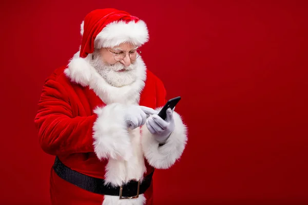 Komik, pozitif, emekli bir adamın fotoğrafı Noel Baba kostüm gözlüğü takıyor modern, boş, izole kırmızı arka plan yazıları yazıyor. — Stok fotoğraf