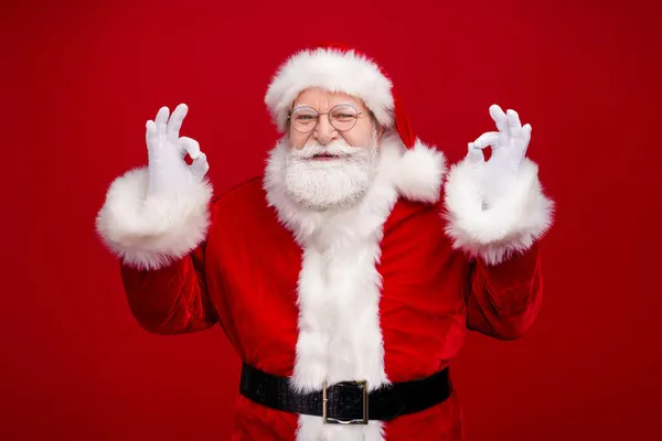 Foto di fiducioso bel pensionato uomo vestito costume di Babbo Natale mostrando segni okey sorridente isolato colore rosso sfondo — Foto Stock