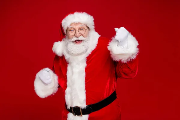 Φωτογραφία του εντυπωσιακού τυχερού συνταξιούχου ντυμένος Άγιος Βασίλης κοστούμι αυξάνεται γροθιές χαμογελώντας απομονωμένο κόκκινο χρώμα φόντο — Φωτογραφία Αρχείου