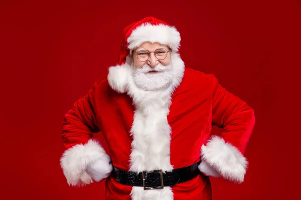 Фото смешного фанки пенсионер носить костюм Санта-Клауса колпак очки улыбающиеся руки руки руки талии изолированный красный цвет фона — стоковое фото