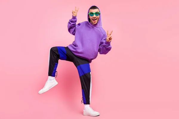 Volledige lengte foto van koele jonge brunet guy dans show v-teken dragen brillen hoodie broek schoenen geïsoleerd op roze achtergrond — Stockfoto