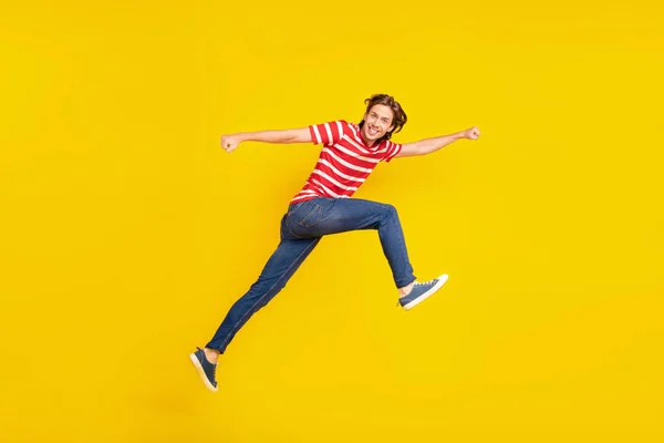 Zdjęcie funky dość młody facet ubrany czerwony t-shirt skoków wysoki uruchomiony szybko uśmiechnięty odizolowany żółty kolor tła — Zdjęcie stockowe