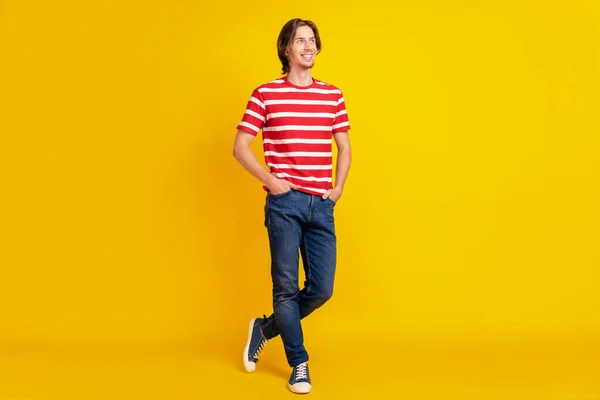 Foto di affascinante bel ragazzo vestito rosso t-shirt camminare tasche del braccio cercando spazio vuoto sorridente isolato colore giallo sfondo — Foto Stock