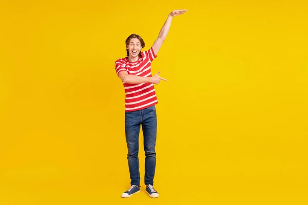멋진 인상을 받은 젊은이의 사진 줄무늬 티셔츠를 입고 손가락으로 빈 공간을 가리키는 크기의 노란 색 배경 사진 — 스톡 사진