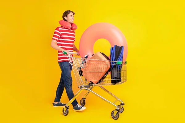 Vista completa del tamaño del cuerpo del atractivo chico alegre que lleva cosas nuevas en el carro aislado sobre fondo de color amarillo brillante — Foto de Stock