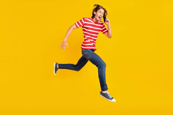 Etkilenmiş yakışıklı bir adamın fotoğrafı çizgili tişört giyiyor, konuşan modern bir cihaz boş, izole edilmiş sarı arkaplan görünümlü. — Stok fotoğraf