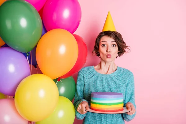 Photo of optimistic curly brunette hairdo lady blow hold balloons cake wear hat blue sweater jeans isolated on pink color background — Stock Photo, Image