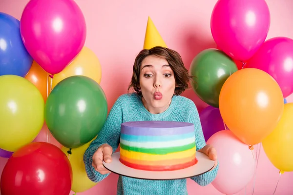 Fotografie slavnostní šťastná žena rána svíčka, aby přání držet dort oblečení kuželové balónky izolované na růžové barevné pozadí — Stock fotografie