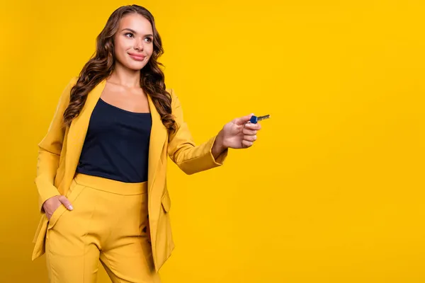 Fotografie okouzlující atraktivní mladá žena oblečená v obleku blejzr s úsměvem ukazující klíč prázdný prostor izolované žluté barvy pozadí — Stock fotografie