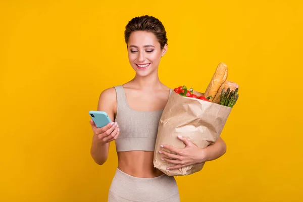 Retrato de menina alegre atraente usando dispositivo de compra de bens alimentação saudável nutrição isolada sobre fundo de cor amarelo brilhante — Fotografia de Stock