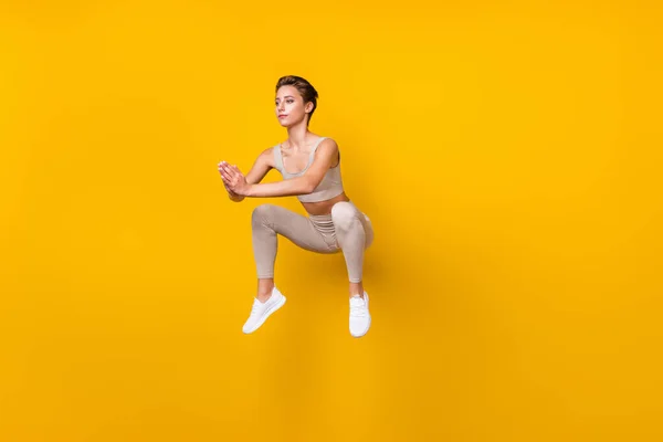 Tam boy vücut ölçüsü: Çekici sportif kız atlama, oturma eylemi, izole edilmiş şekilde oturma, parlak sarı arka plan üzerinde çalışma. — Stok fotoğraf