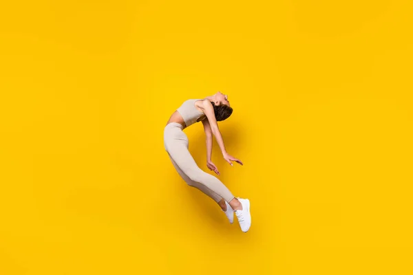 Фото беззаботной радостной дамы прыгать гибкая поза носить обрезанные верхние леггинсы обувь изолированный желтый цвет фона — стоковое фото