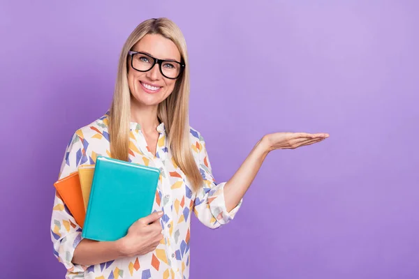 Foto de bastante lindo señora madura vestida impresión blusa gafas sosteniendo brazo espacio vacío copybooks aislado color púrpura fondo —  Fotos de Stock