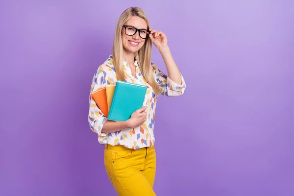 Photo of charming smart young woman wear print shirt spectacles smiling holding book stack empty space isolated violet color background — Stock Photo, Image