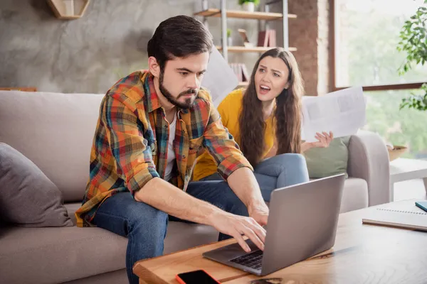 Foto de jóvenes amantes irritados infelices vestidos ropa casual mecanografía gadget moderno gritando la celebración de documentos en el interior apartamento loft — Foto de Stock