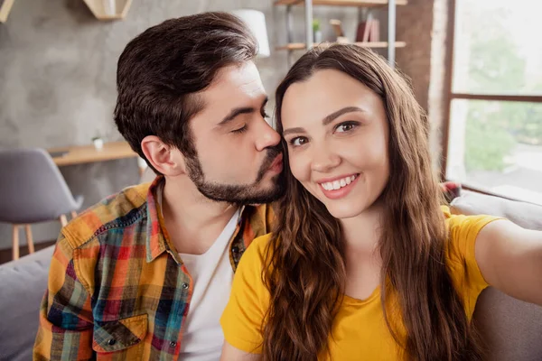 Photo of romantic adorable young lovers dressed casual clothes tacking selfie kissing cheekbone smiling indoors loft apartment — Stock Photo, Image
