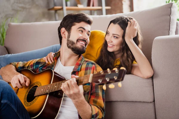 Foto av söta attraktiva unga par bär casual outfits sittande soffa spela gitarr lyssna sång inomhus hus rum — Stockfoto