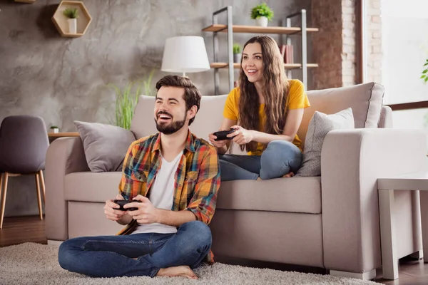 Foto di divertente funky giovane coppia indossare abiti casual sorridente seduta divano tenendo playstation gamepad all'interno della stanza della casa — Foto Stock
