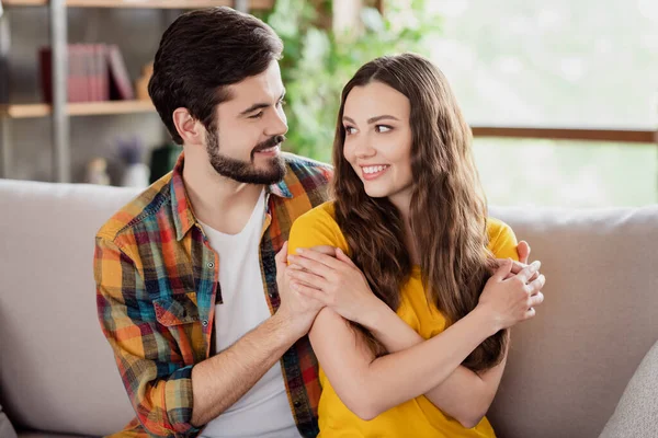 Foto de doce terno jovens amantes vestidos roupas casuais sentado sofá sorrindo abraçando os olhos olhando dentro de casa apartamento loft — Fotografia de Stock