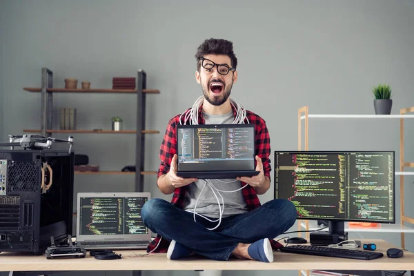 Πορτρέτο του ελκυστικού απελπισμένου χάκερ που κάθεται στο τραπέζι κρατώντας το laptop code βάση δεδομένων στο χώρο εργασίας σε εσωτερικούς χώρους — Φωτογραφία Αρχείου