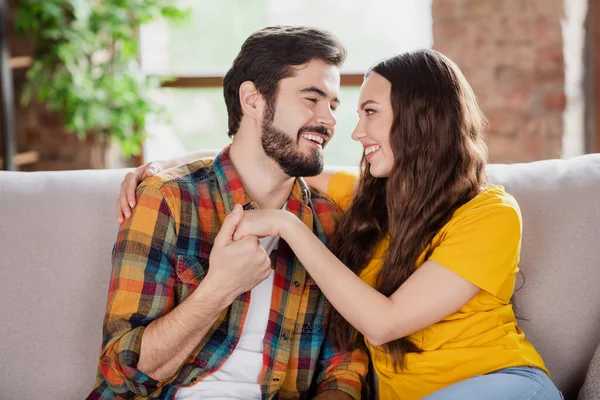Photo of dreamy sweet young lovers dressed casual clothes sitting sofa smiling holding arms looking eyes indoors loft apartment — Stock Photo, Image