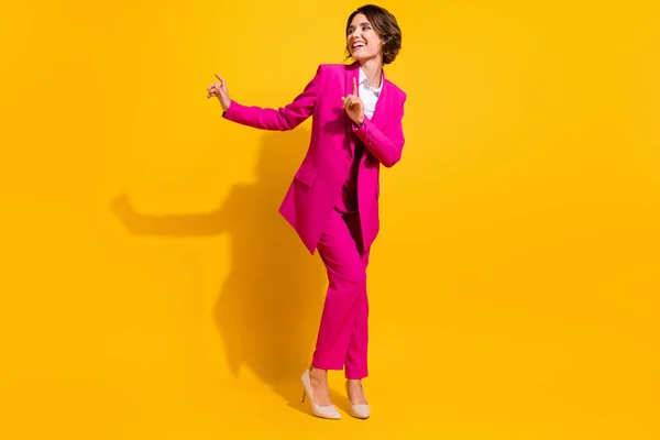 Фото очаровательной модной молодой женщины, одетой в розовый костюм, танцующей на изолированном желтом фоне — стоковое фото