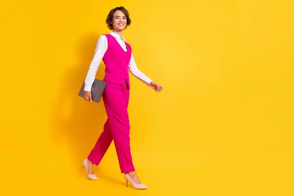 Фото блестящей очаровательной юной леди в розовом костюме, держащей в руках современное устройство, ходящее пустое пространство, улыбающееся изолированно желтым цветом фона — стоковое фото